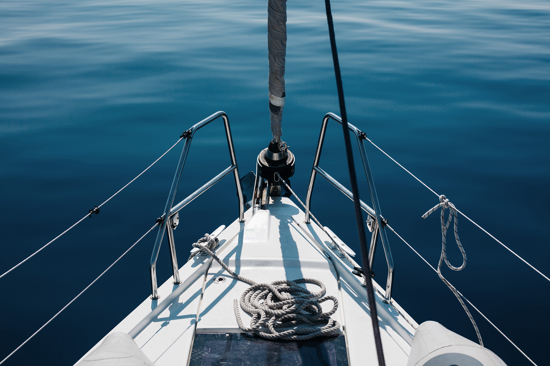 Bug einer Yacht mit Reling und Seilen. Im Hintergrund blaues Wasser.